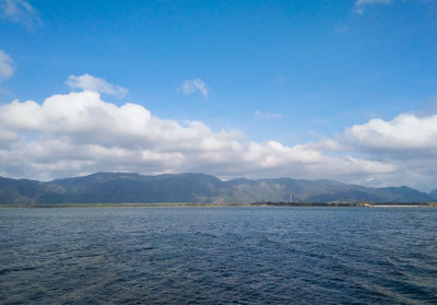 Scenic view of sea by mountain against sky