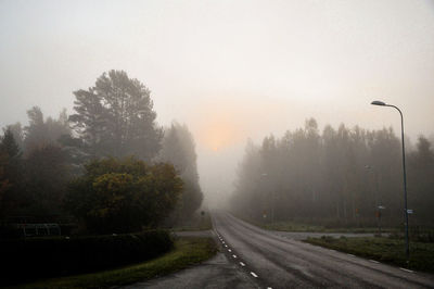 Road by trees against sky during foggy weather