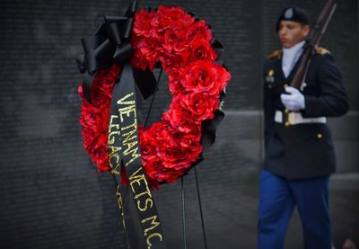 Close-up of red wreath with army soldier standing in background