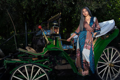 Sensuous woman standing in carriage against trees