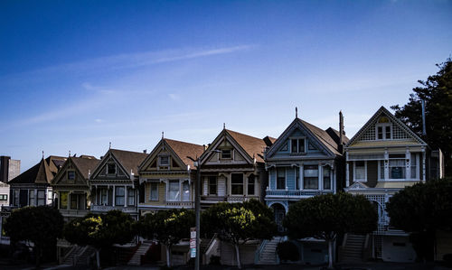 Houses by trees and buildings against blue sky