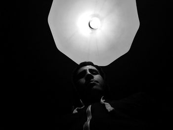 Low angle view of man with illuminated light bulb in darkroom