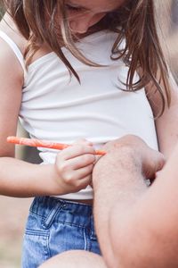 Daughter writing on fathers hand using orange felt tip pen