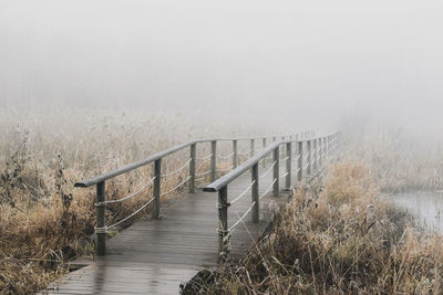 Wooden railing by frozen lake against sky during winter