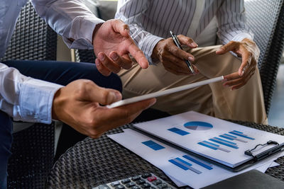 Midsection of business colleagues discussing over digital tablet while sitting on chairs in office