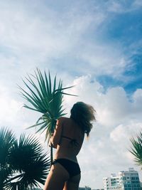 Low angle view of woman standing by palm tree against sky