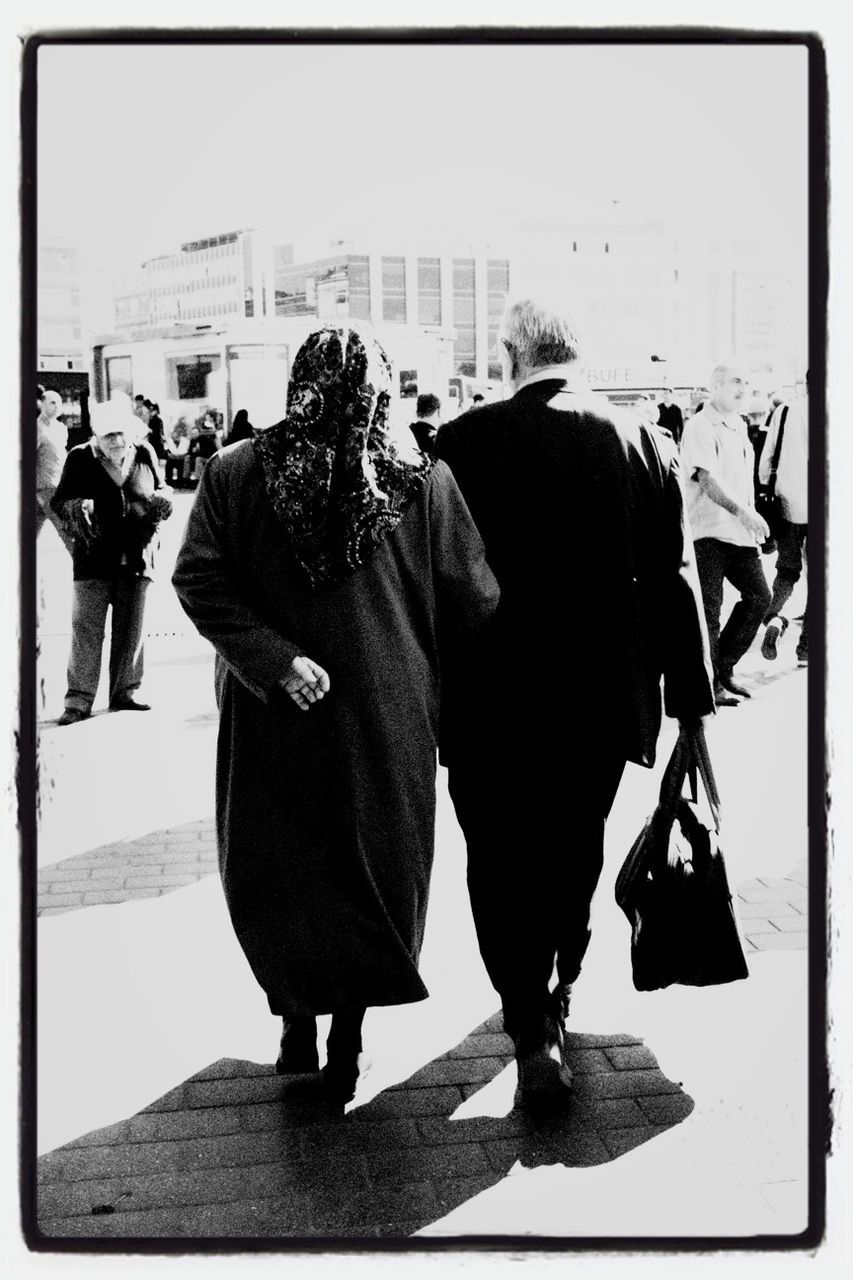 men, transfer print, rear view, full length, lifestyles, walking, person, auto post production filter, casual clothing, standing, leisure activity, city, building exterior, city life, street, togetherness, built structure