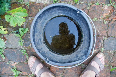 Low section of man standing by bucket on footpath