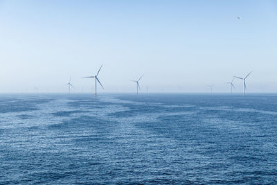 A cluster of turbines of a wind farm on the blue glittering sea under a cloudless blue sky