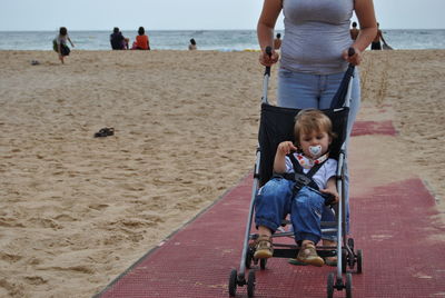 Low section of woman with son in baby stroller at beach