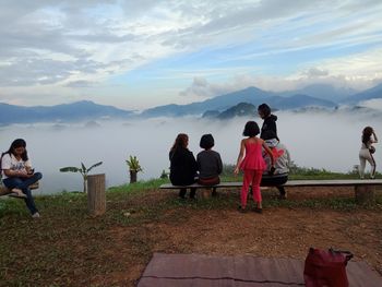 People sitting on seat at mountain against sky