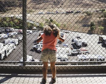 Rear view of girl standing by chainlink fence on sunny day