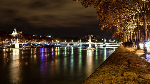 Illuminated city by river against sky at night