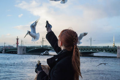 Red hair young woman feeding birds on embankment