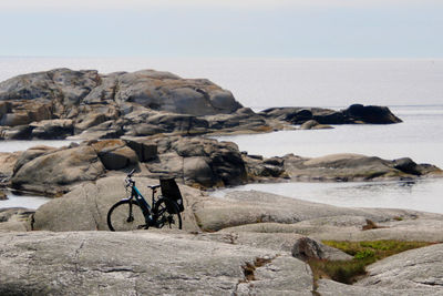 Bicycle on rocks by sea against sky