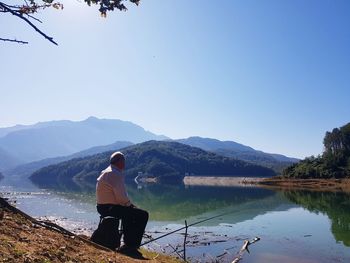 Rear view of man looking at lake against sky