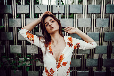 Portrait of woman with arms raised standing against fence