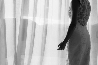 Rear view of woman standing by window at home