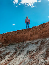 Low angle view of man standing on rock against blue sky