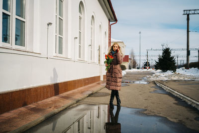 Girl at the train station is talking on a smartphone, a bouquet of tulip flowers in her hands