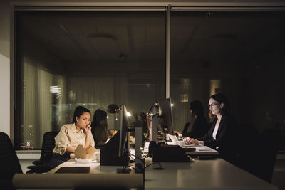 Multiracial female colleagues working late night at desk in office