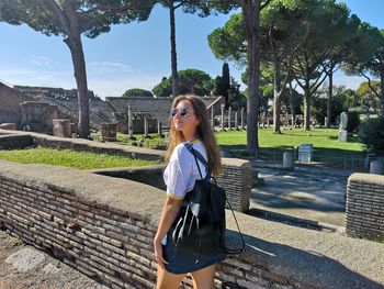 Side view of young woman with backpack standing by retaining wall in park
