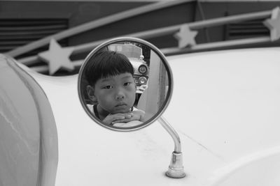 Portrait of cute boy seen in side-view mirror of car