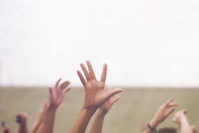 Cropped hands of people with arms raised against clear sky