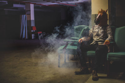 Man with horse head sitting in a smoky basement