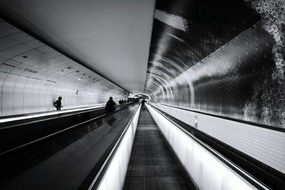 Silhouette people on moving walkway at subway station