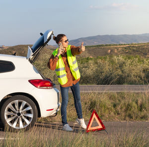 Man sticking his finger out hitchhiking after his car breaks down and talks on phone with insurance