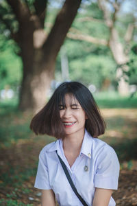 Smiling young woman tossing hair while sitting at park