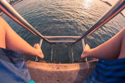 Low section of person sitting on ladder by lake