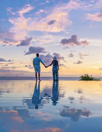 Rear view of man standing at beach against sky during sunset