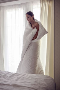 Young woman in a white towel after a spa is standing in the room at the door with tea in her hands