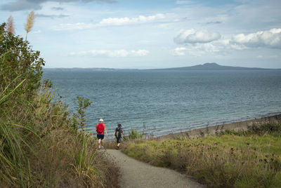 Rear view of people walking on shore by sea against sky
