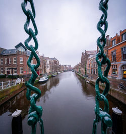 Bridge over river amidst buildings in city against sky