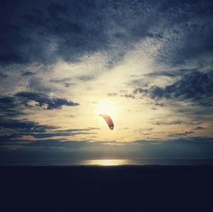 People paragliding over sea during sunset