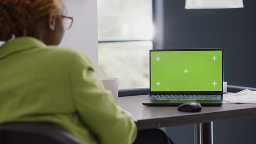 Rear view of woman using laptop at home