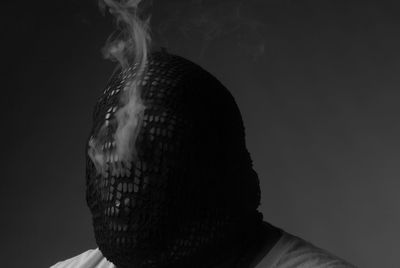 Close-up of man wearing mask smoking against gray background