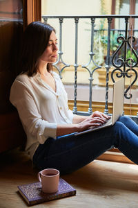 Young woman working from home with a laptop next to a window.
