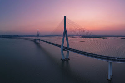 Suspension bridge over sea against sky during sunset