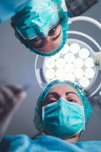 From below female surgeons in medical uniform using professional tools while standing under bright light in operating theater