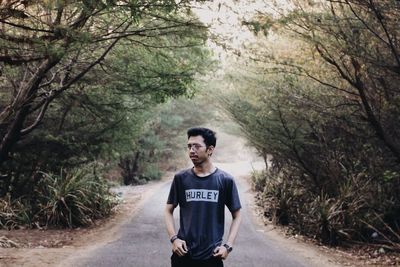 Young man standing on road in forest