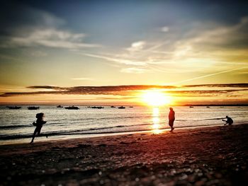 People at beach against sky during sunset