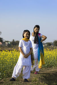 A beautiful indian woman and her daughter in white dress standing near yellow mustard flower field