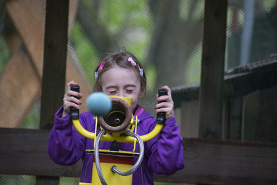 Portrait of a girl holding camera while standing by fence