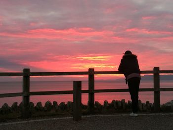 Silhouette man standing by railing against sea during sunset