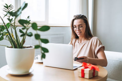 Young woman in glasses doing online shopping on laptop at home