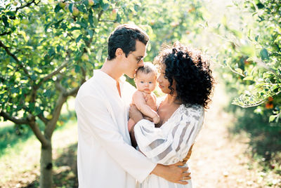 Side view of young couple standing against trees